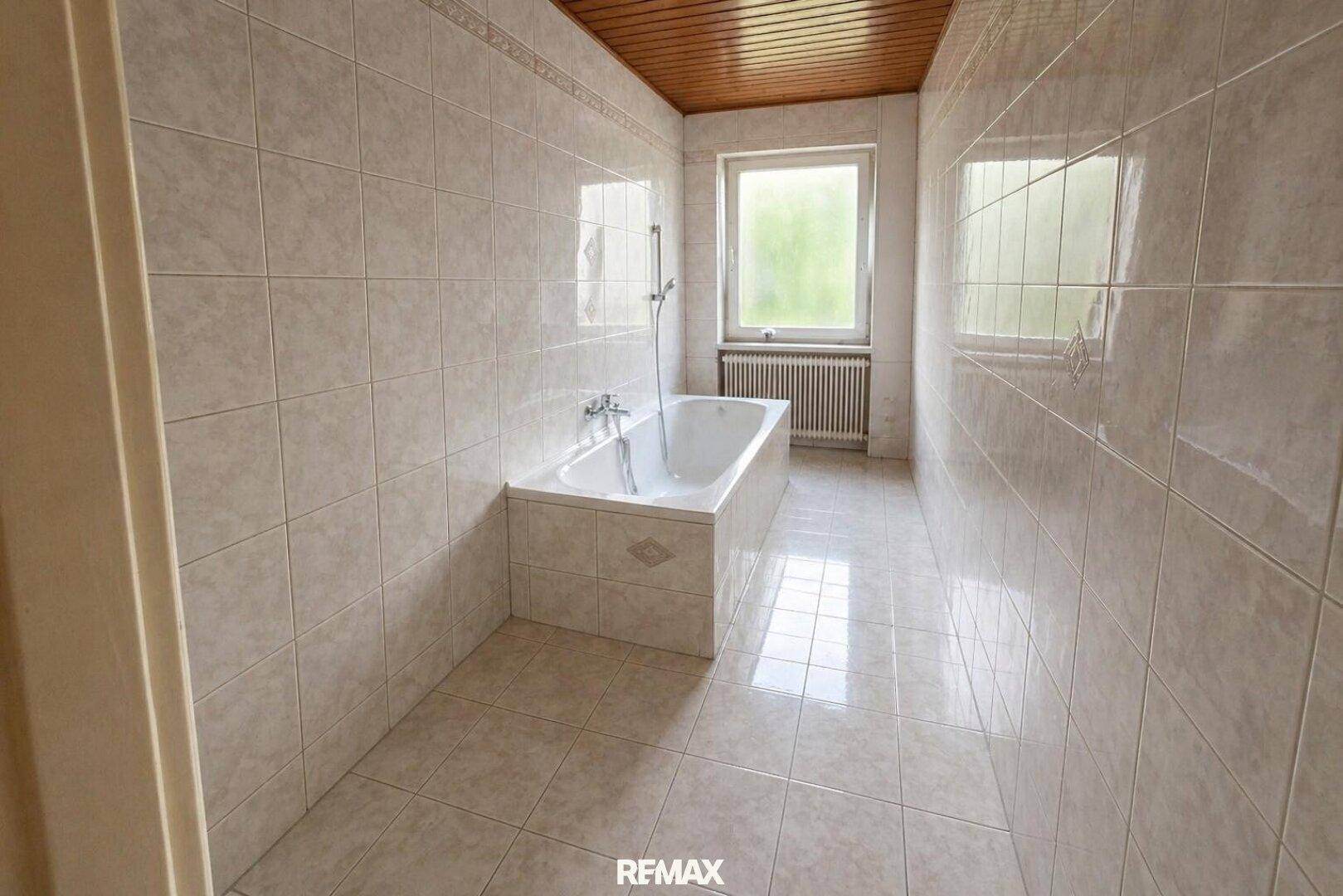 Helles Badezimmer mit Badewanne, Fliesenwänden und Holzdecke.