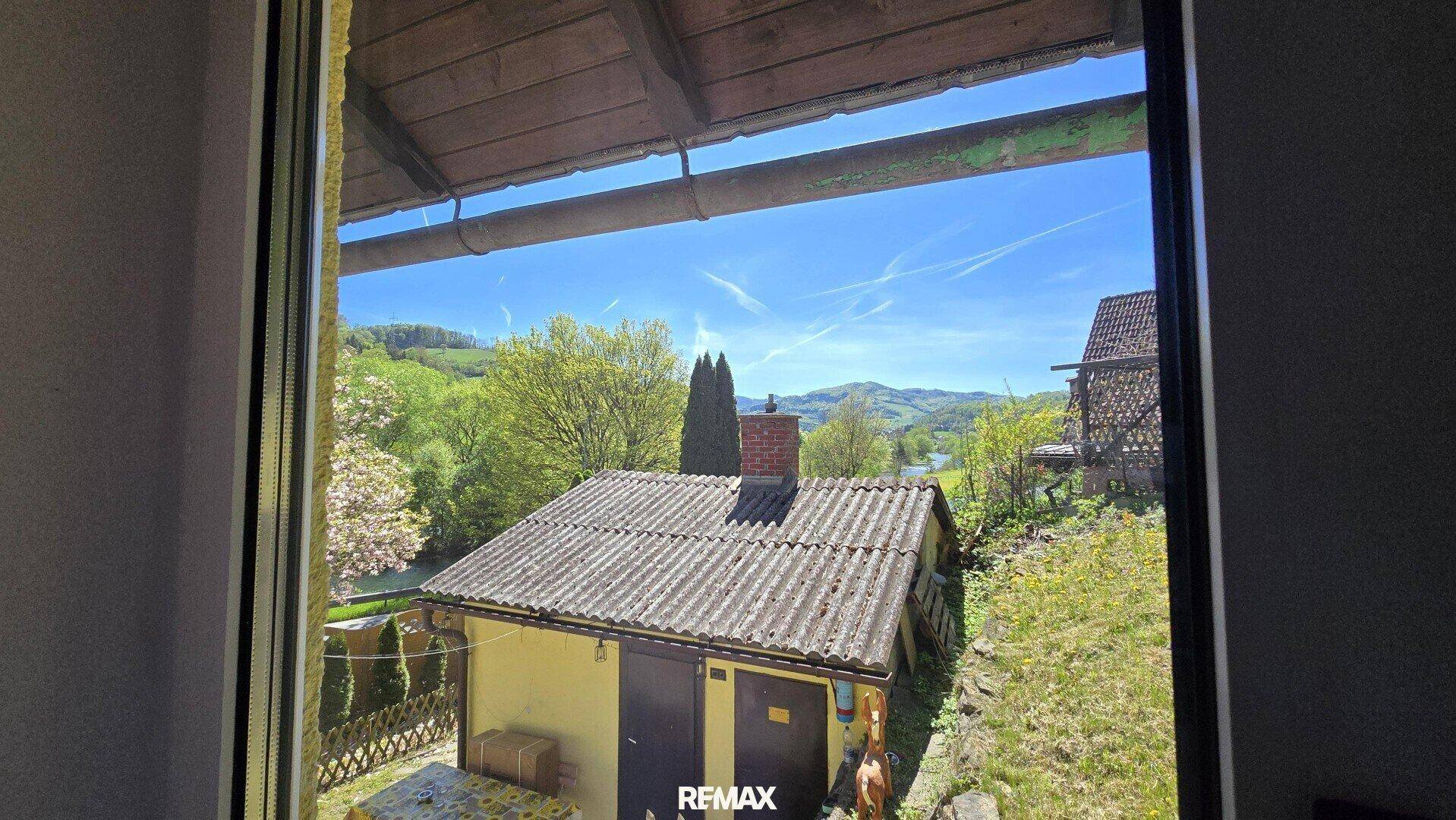 Blick aus dem Fenster auf ein Nebengebäude und die umliegende grüne Landschaft.