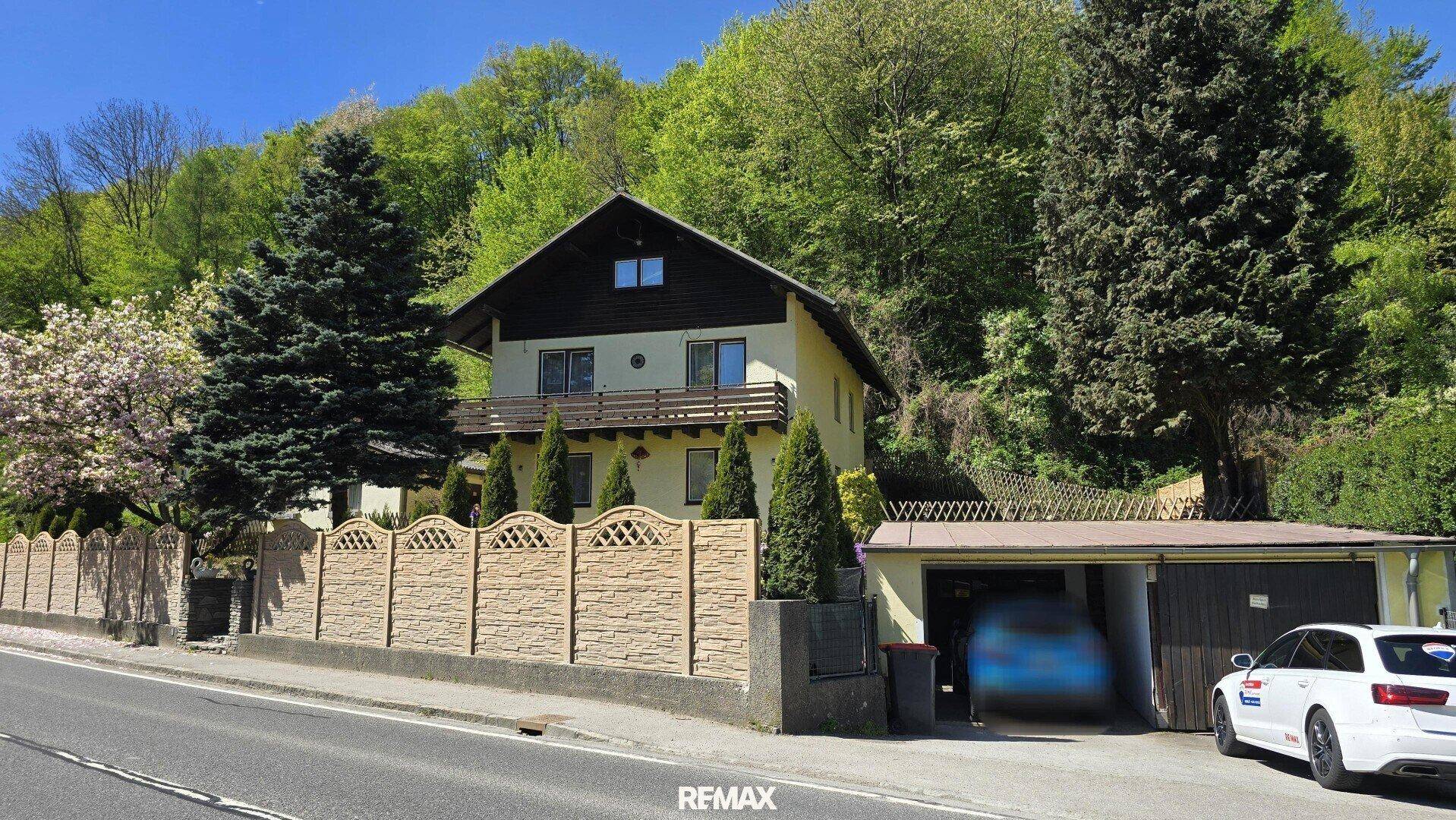 Haus mit Garage und Zaun, direkt an einer Straße gelegen, umgeben von Natur.