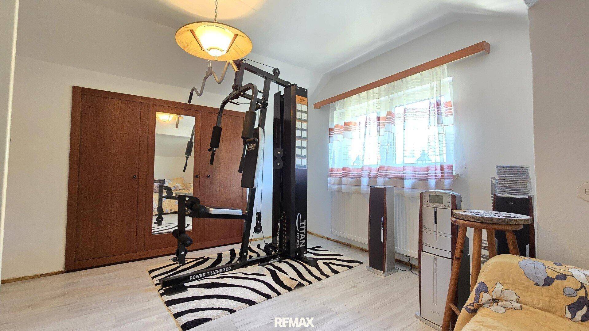 Raum mit Fitnessgerät, Holzschrank und Fenster mit Vorhängen.