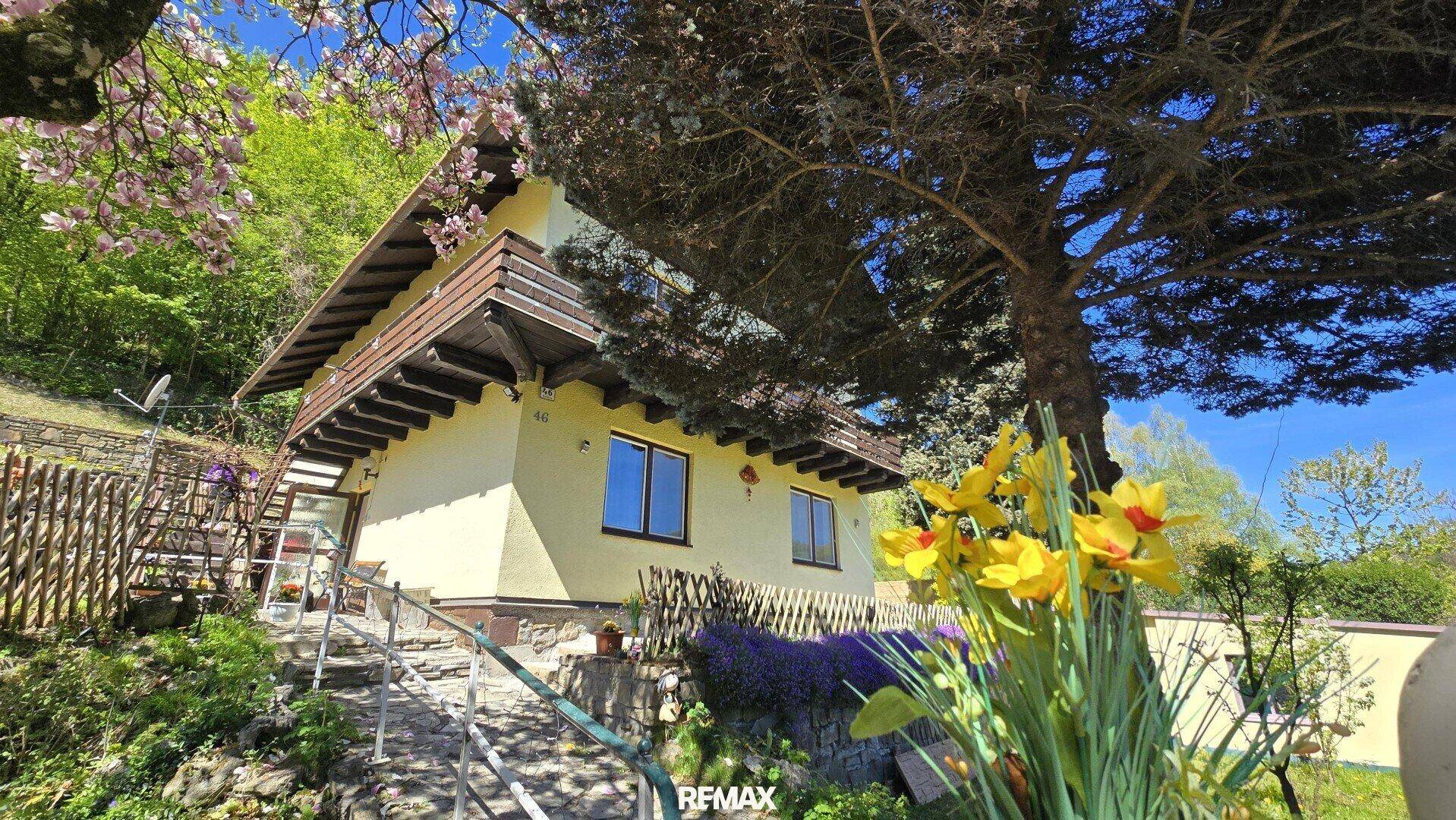 Hausfassade mit blühenden Bäumen und einem gepflegten Gartenbereich.