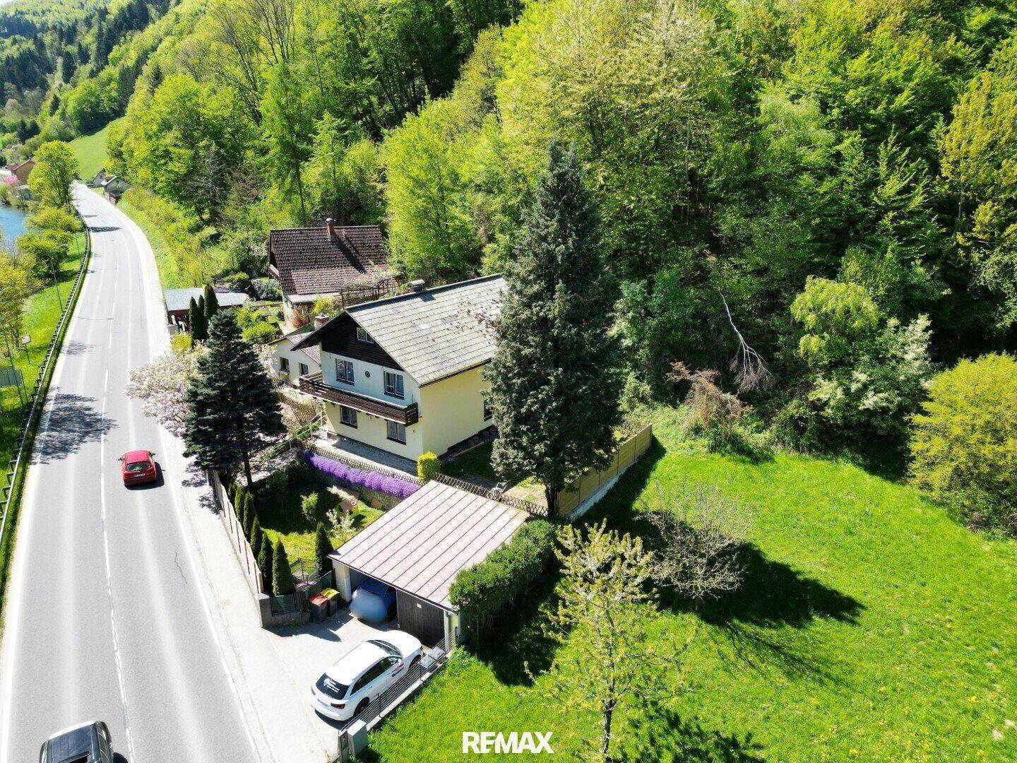 Luftaufnahme des Hauses mit Garage, umgeben von Wald und einer Landstraße.