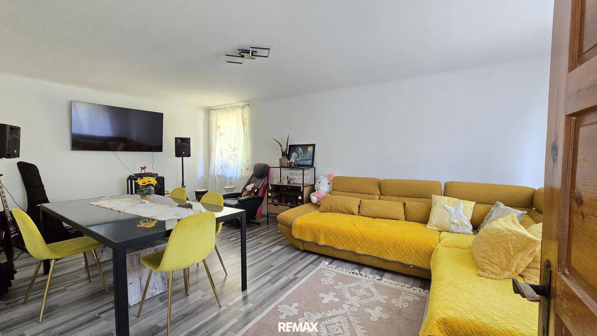 Gemütlicher Wohn- und Essbereich mit gelbem Sofa, modernem Esstisch und Laminatboden.
