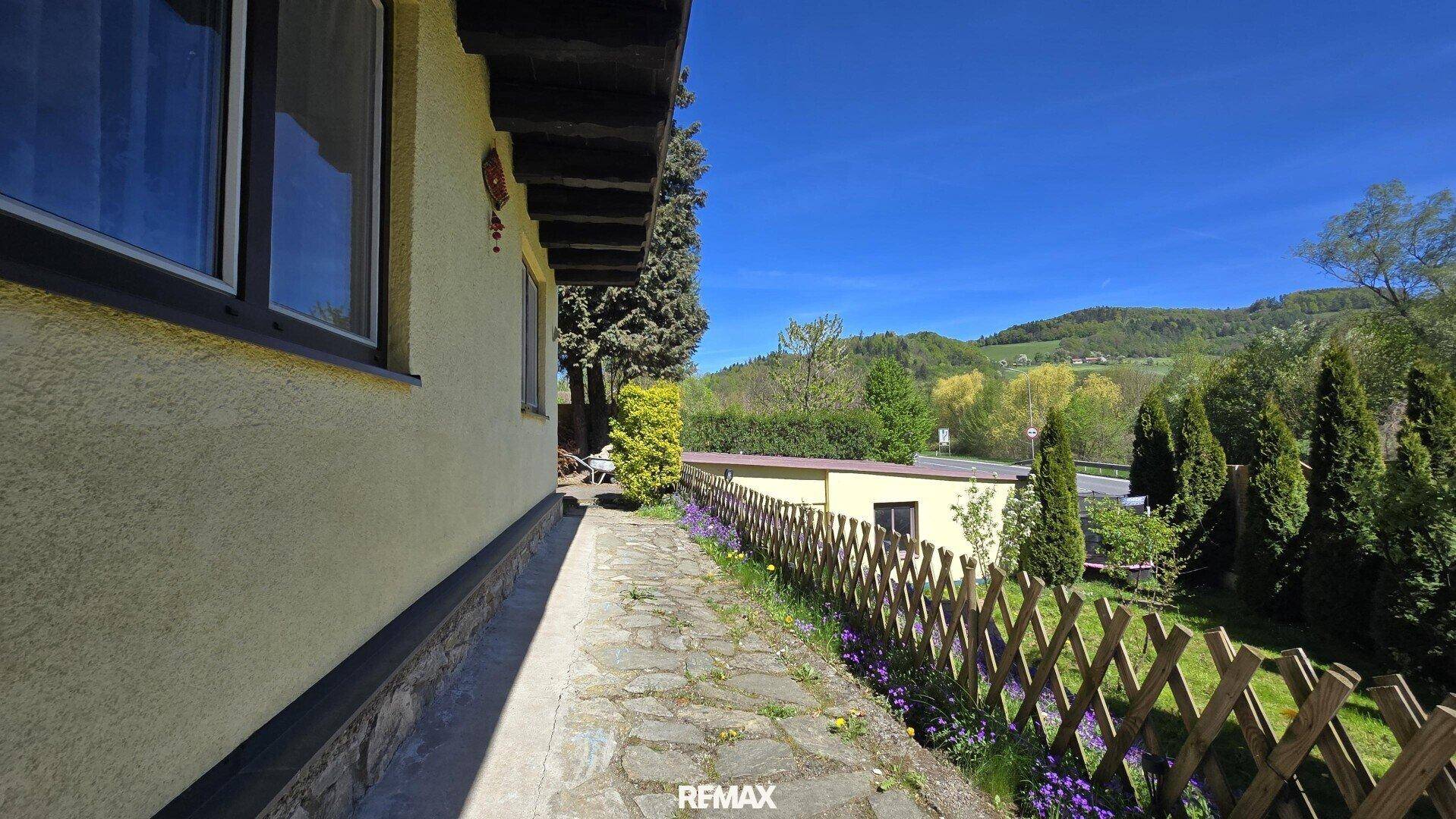 Gartenweg entlang der Hausseite mit Blumen und Blick auf die Landschaft.