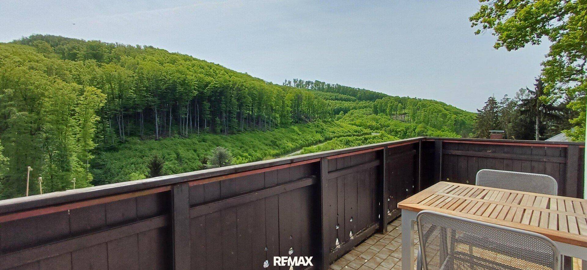 Balkon mit Holzboden und Möbeln, bietet einen weiten Blick auf die bewaldeten Hügel.