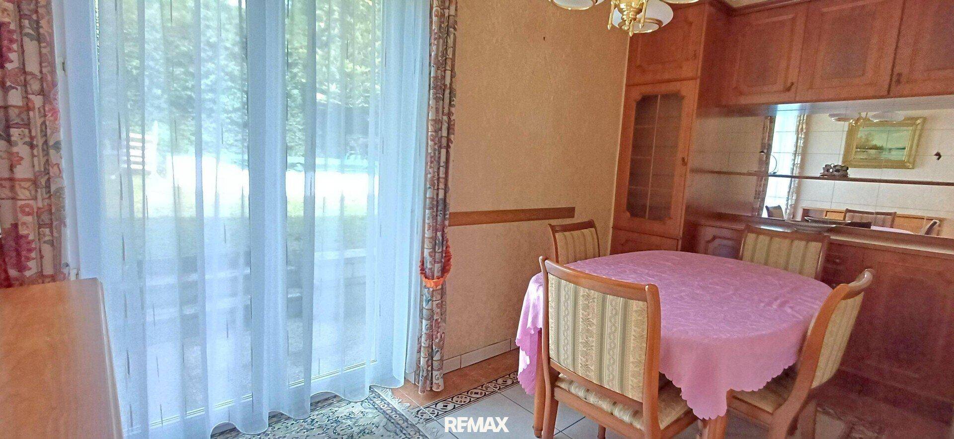 Heller Essbereich mit rundem Tisch, Stühlen und Zugang zu einem Außenbereich durch große Fenster.