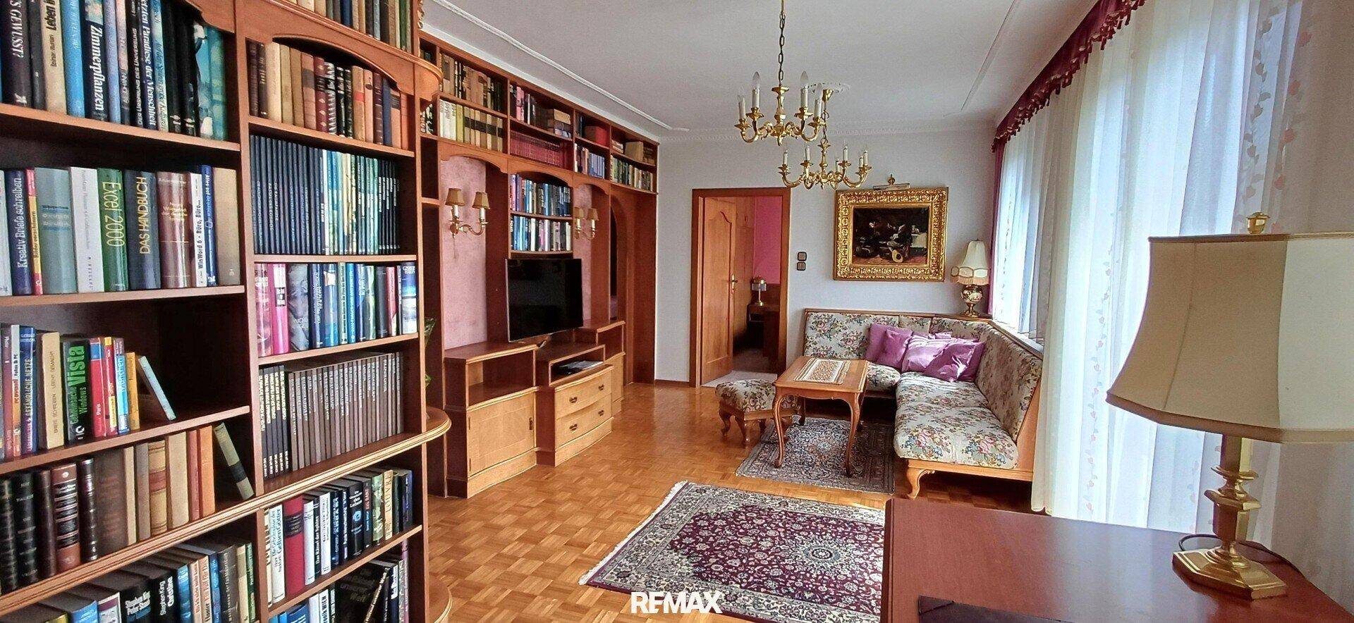 Geräumiges Wohnzimmer mit umfangreichen Bücherregalen, bequemen Sofas und einem eleganten Kronleuchter.