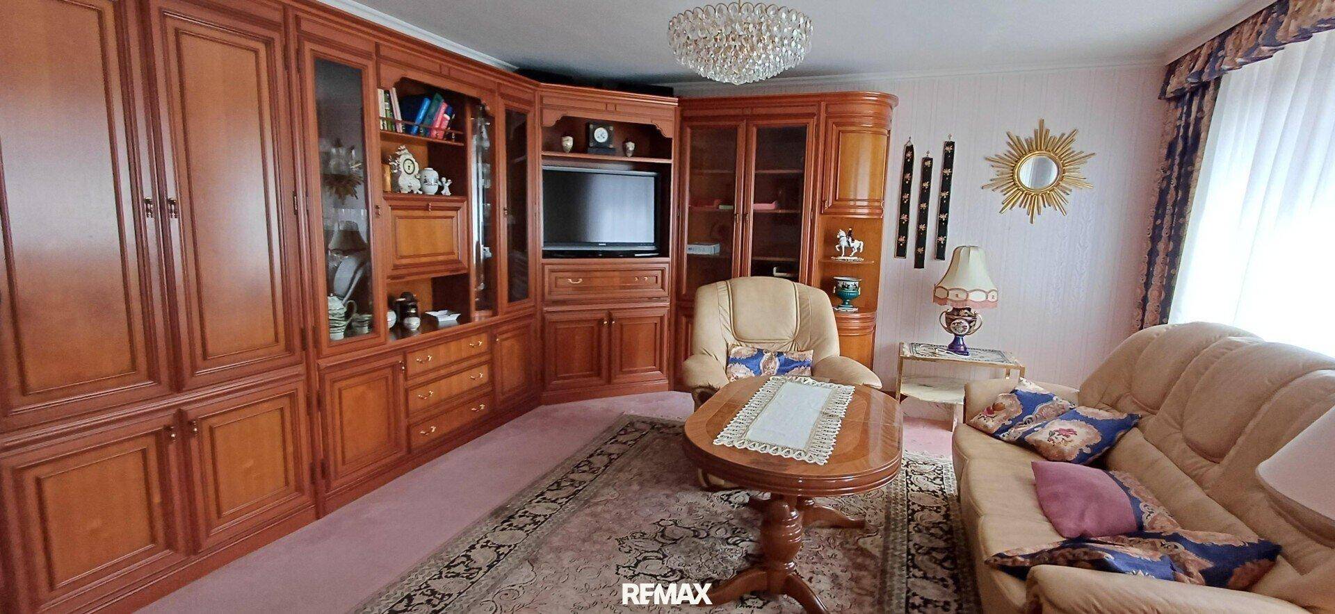 Traditionelles Wohnzimmer mit großen Holzschränken, beigem Sofa und einem Kronleuchter.