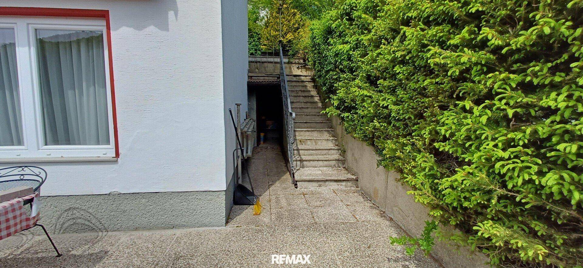 Gepflasterter Weg neben dem Haus mit Treppe, die zu einem höher gelegenen Bereich führt.
