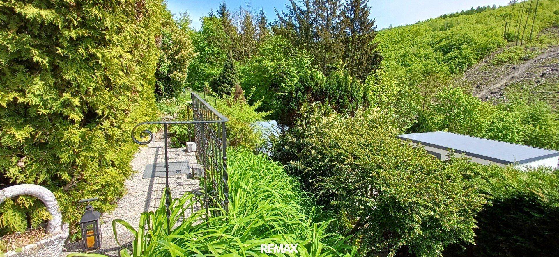 Gartenweg mit schmiedeeisernem Geländer und weitem Blick auf die grüne Hügellandschaft.