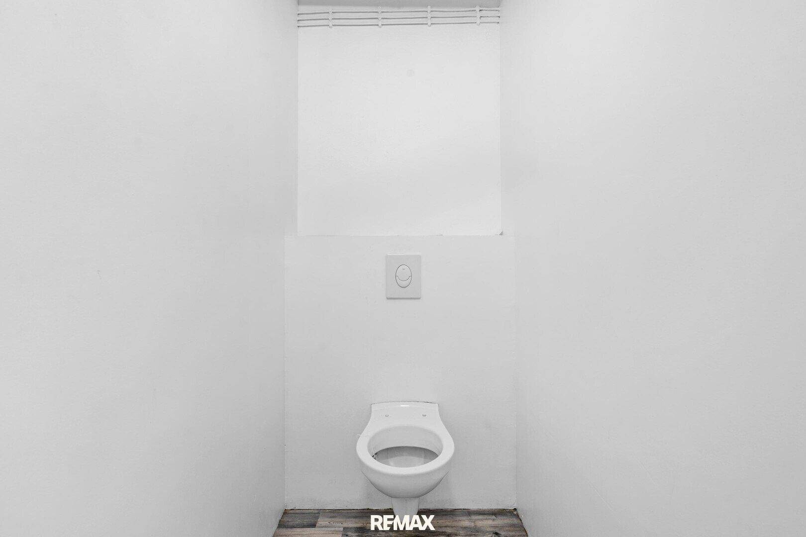 Kleiner Toilettenraum mit wandhängendem WC und Laminatboden in Holzoptik.