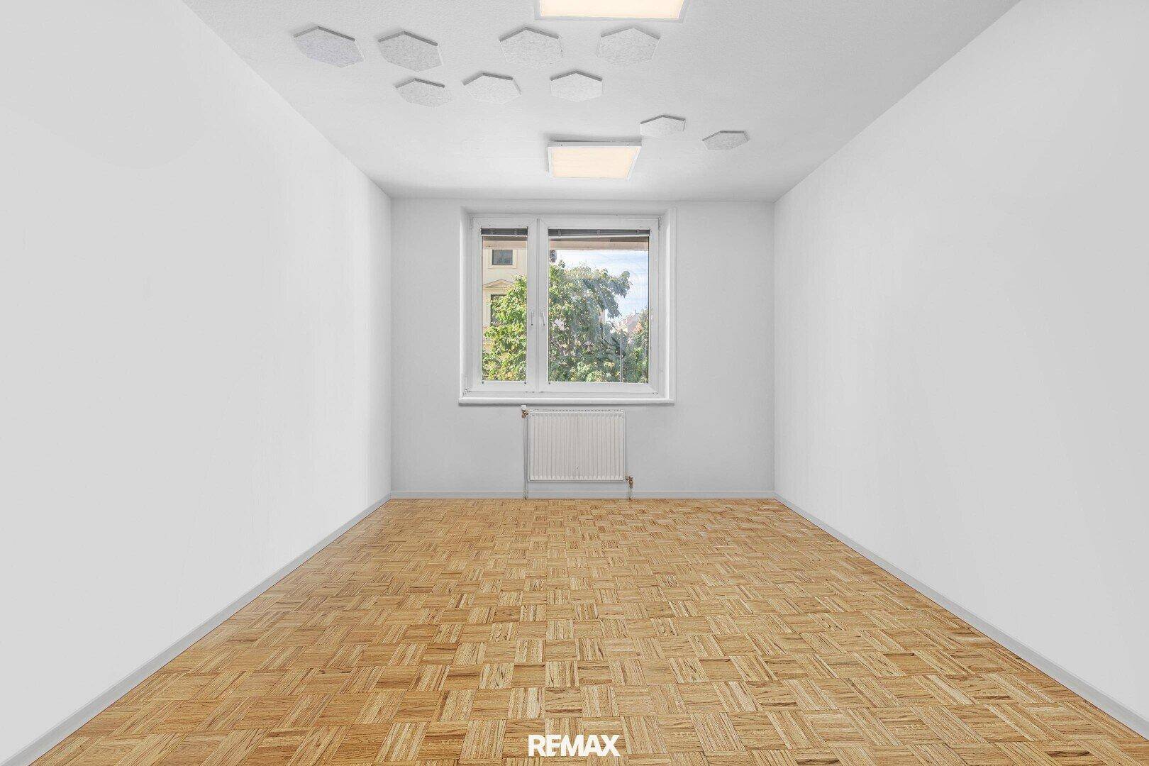Leeres Zimmer mit Parkettboden, weißen Wänden und einem Fenster, das Tageslicht hereinlässt.