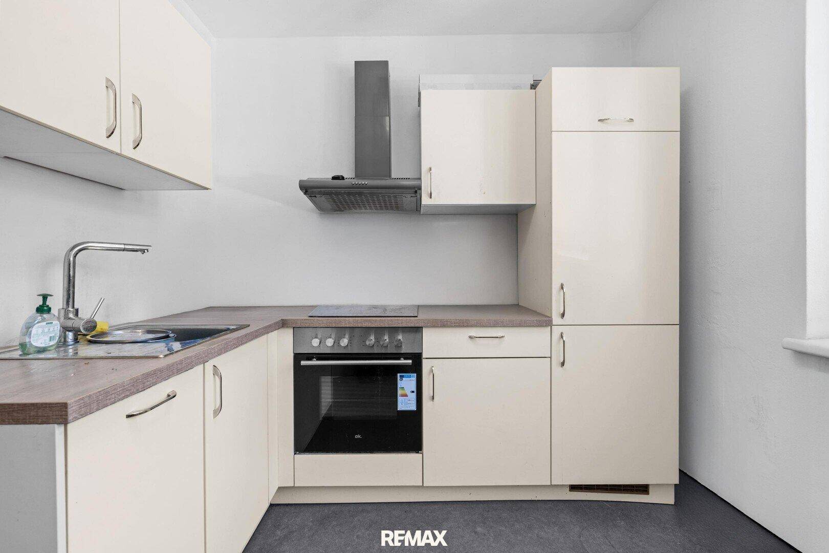 Funktionale Küche mit beigefarbenen Schränken, integriertem Backofen und Dunstabzugshaube.