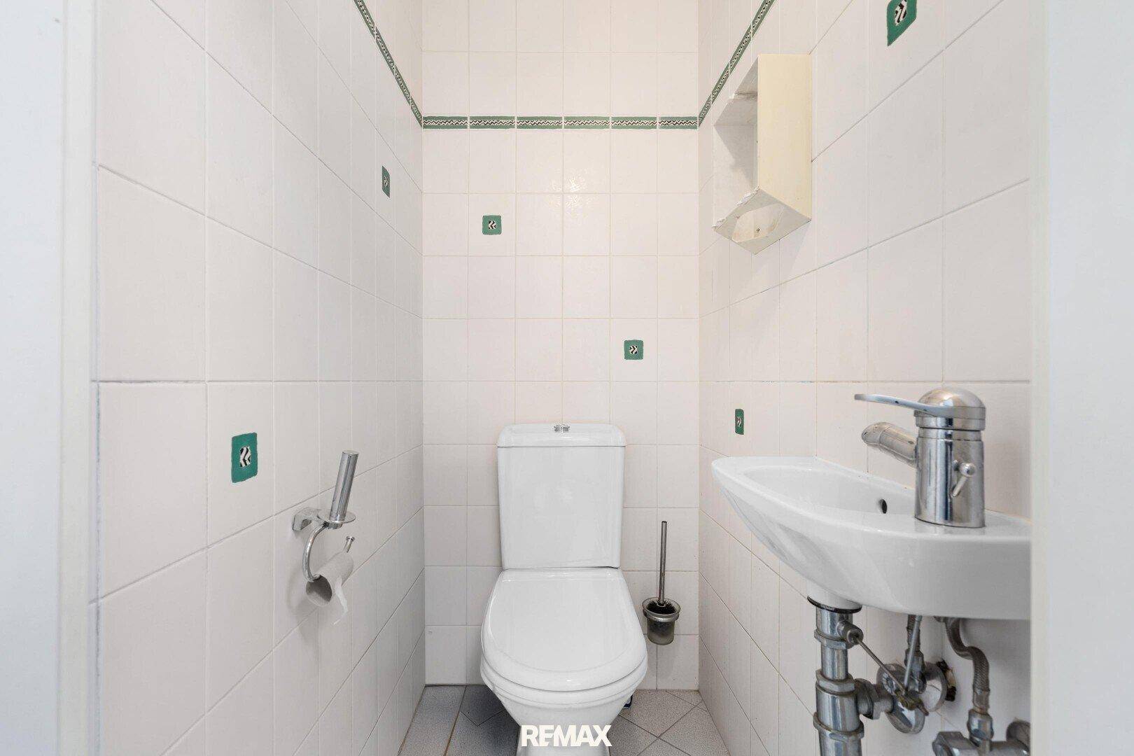 Kleiner Toilettenraum mit weißen Fliesen, WC und einem kompakten Waschbecken.
