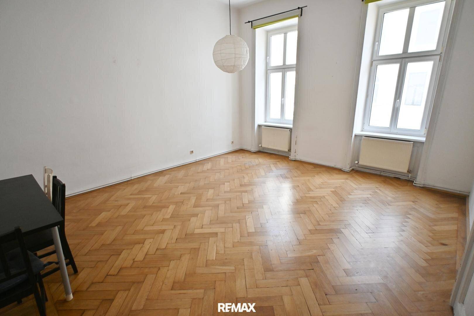 Helles Zimmer mit Fischgrätparkett und hohen Fenstern, ideal als Wohnbereich.