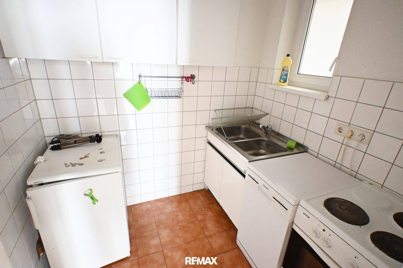 Kompakte Küche mit weißen Fliesen und grundlegenden Geräten, ideal für den täglichen Gebrauch.