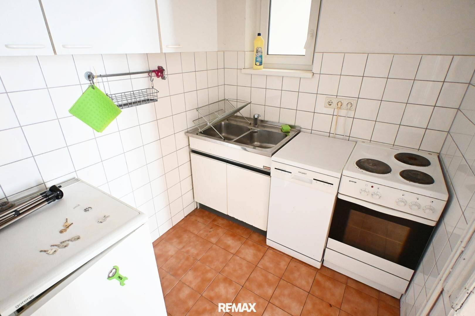 Kleine Küche mit weißen Fliesen, einfacher Ausstattung und Fenster, funktional und hell.