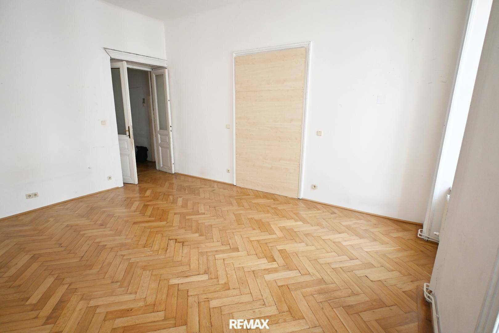 Geräumiges Zimmer mit Fischgrätparkett und offenem Zugang zu weiteren Räumen, mit viel Potenzial.