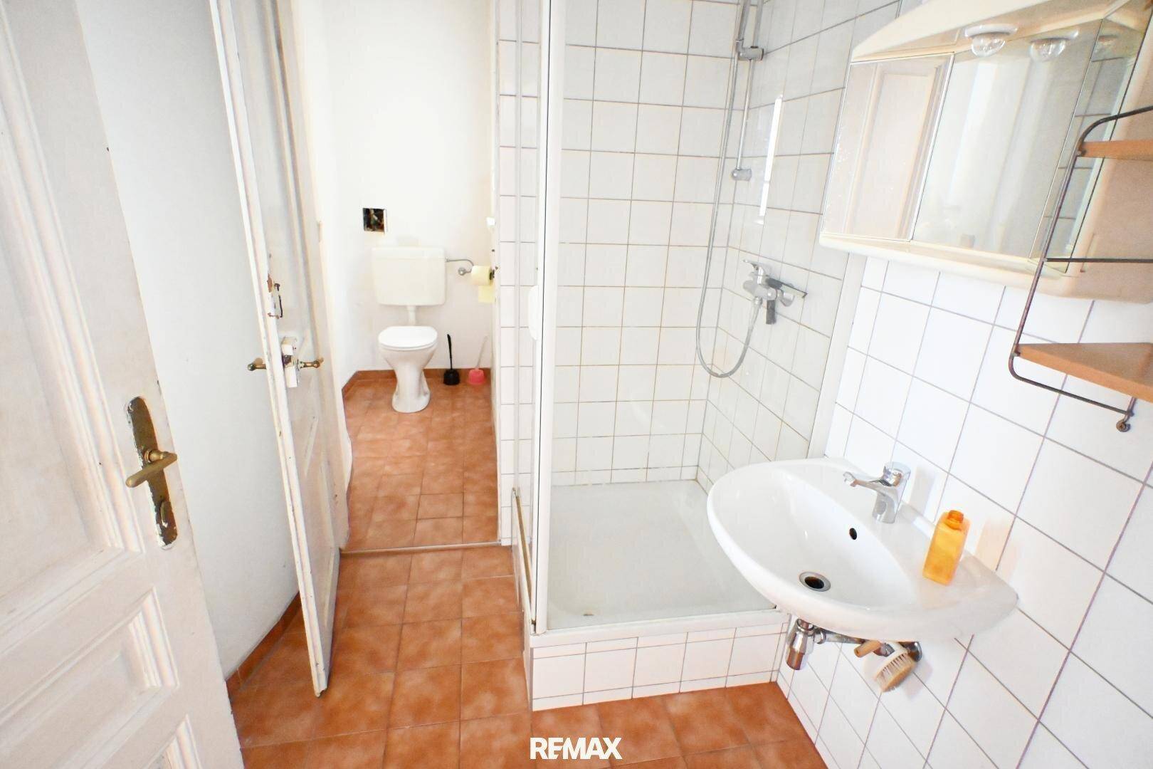 Badezimmer mit Dusche, Waschbecken und Zugang zur separaten Toilette, einfach und funktional.