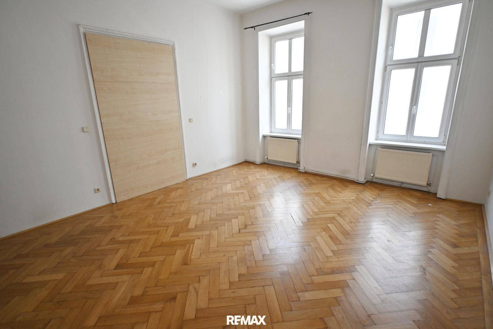 Helles Zimmer mit Fischgrätparkett und einer modernen Holztür, bietet vielseitige Nutzungsmöglichkeiten.