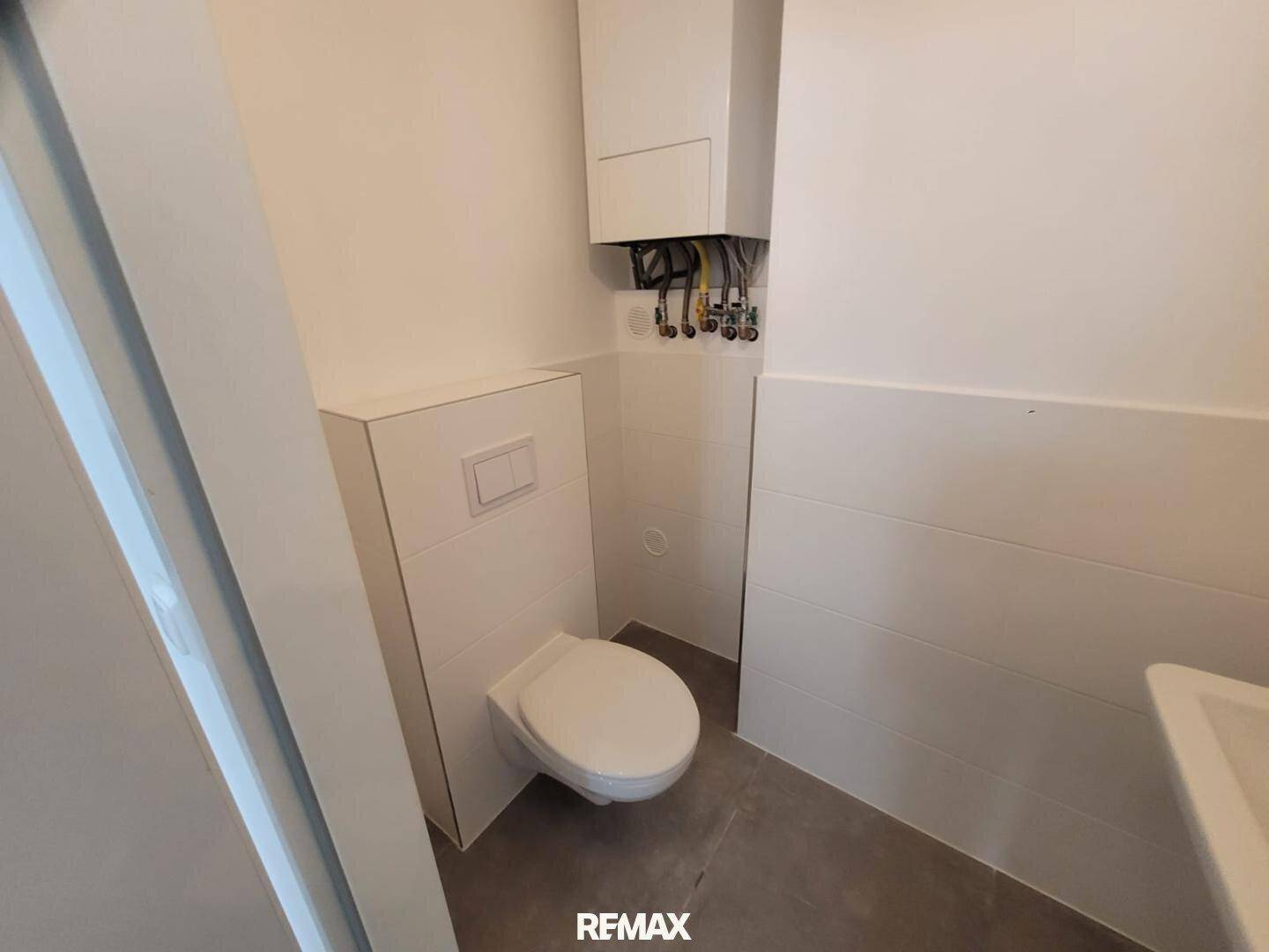 Separates WC mit wandhängender Toilette, kleinem Waschbecken und Gastherme an der Wand.