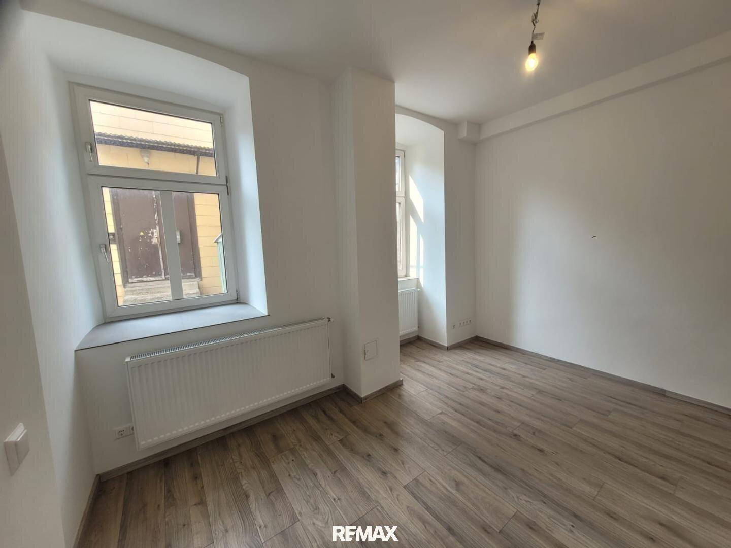 Heller Raum mit Laminatboden und einem großen Fenster, das viel Tageslicht hereinlässt.