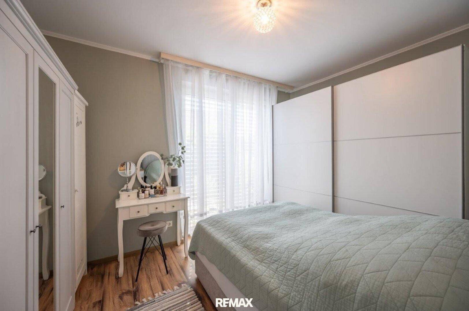 Helles Schlafzimmer mit Holzboden, großem Kleiderschrank und Schminktisch am Fenster.