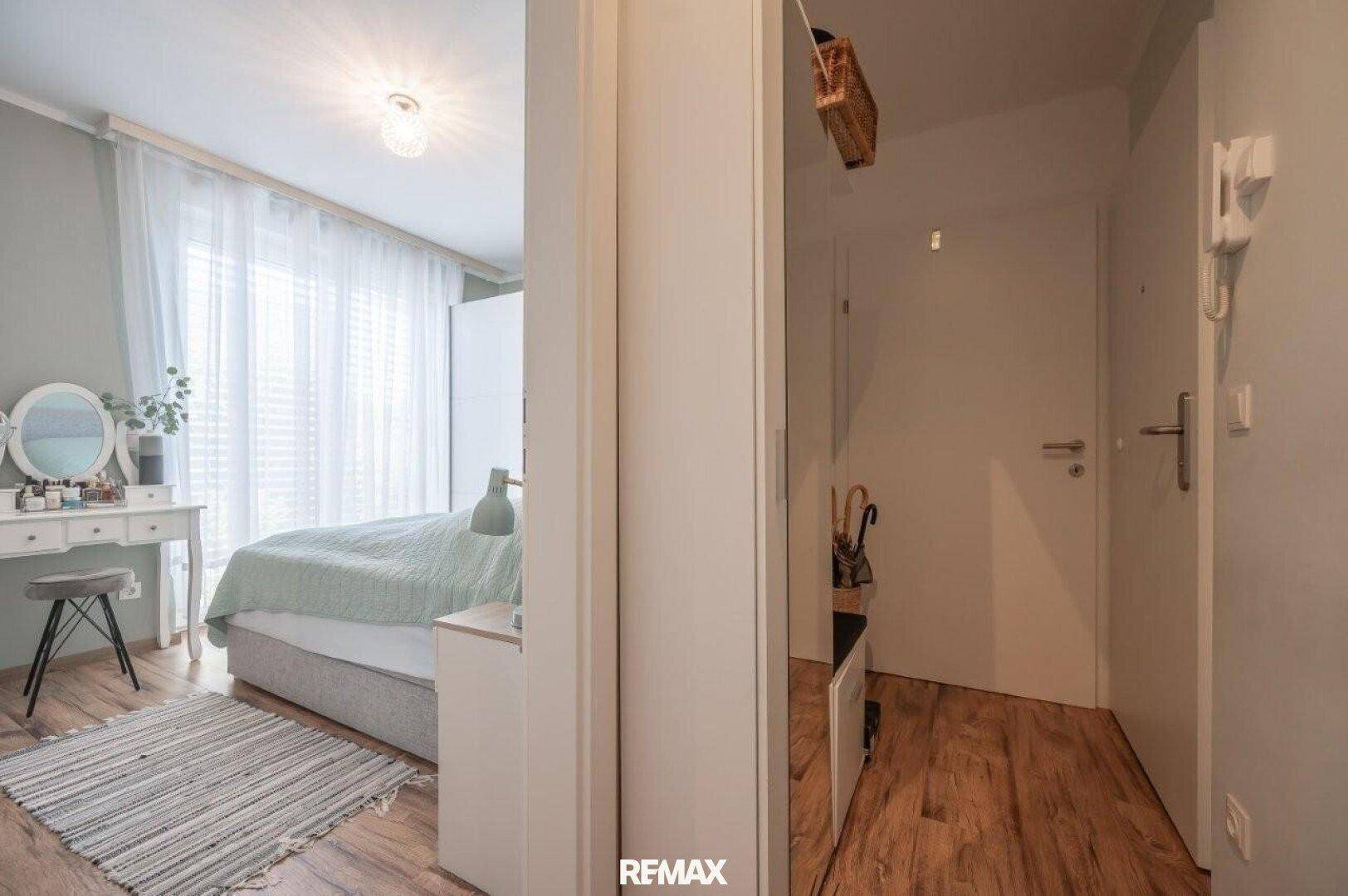Heller Flur mit Holzboden und Zugang zu einem Schlafzimmer mit Schminktisch.