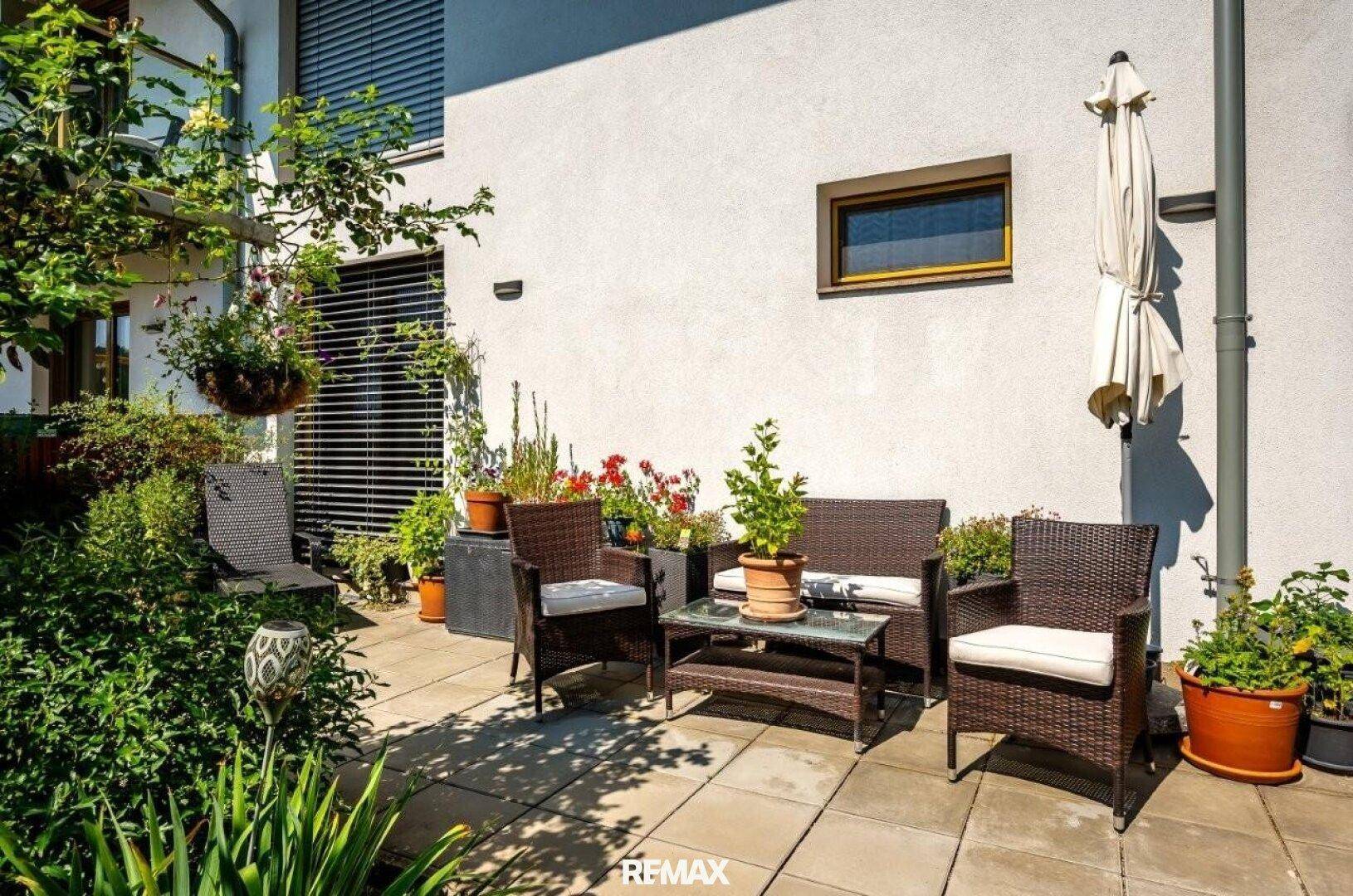 Gemütliche Terrasse mit Gartenmöbeln, Sonnenschirm und vielen Topfpflanzen.