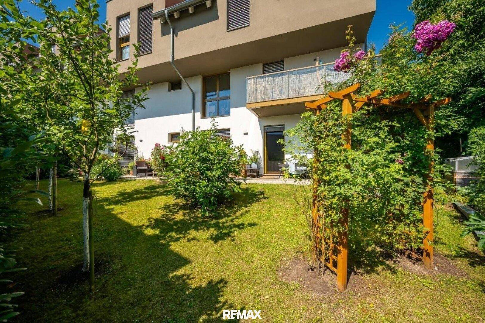 Rückseite des Gebäudes mit gepflegtem Garten, Rasenfläche und blühenden Pflanzen.