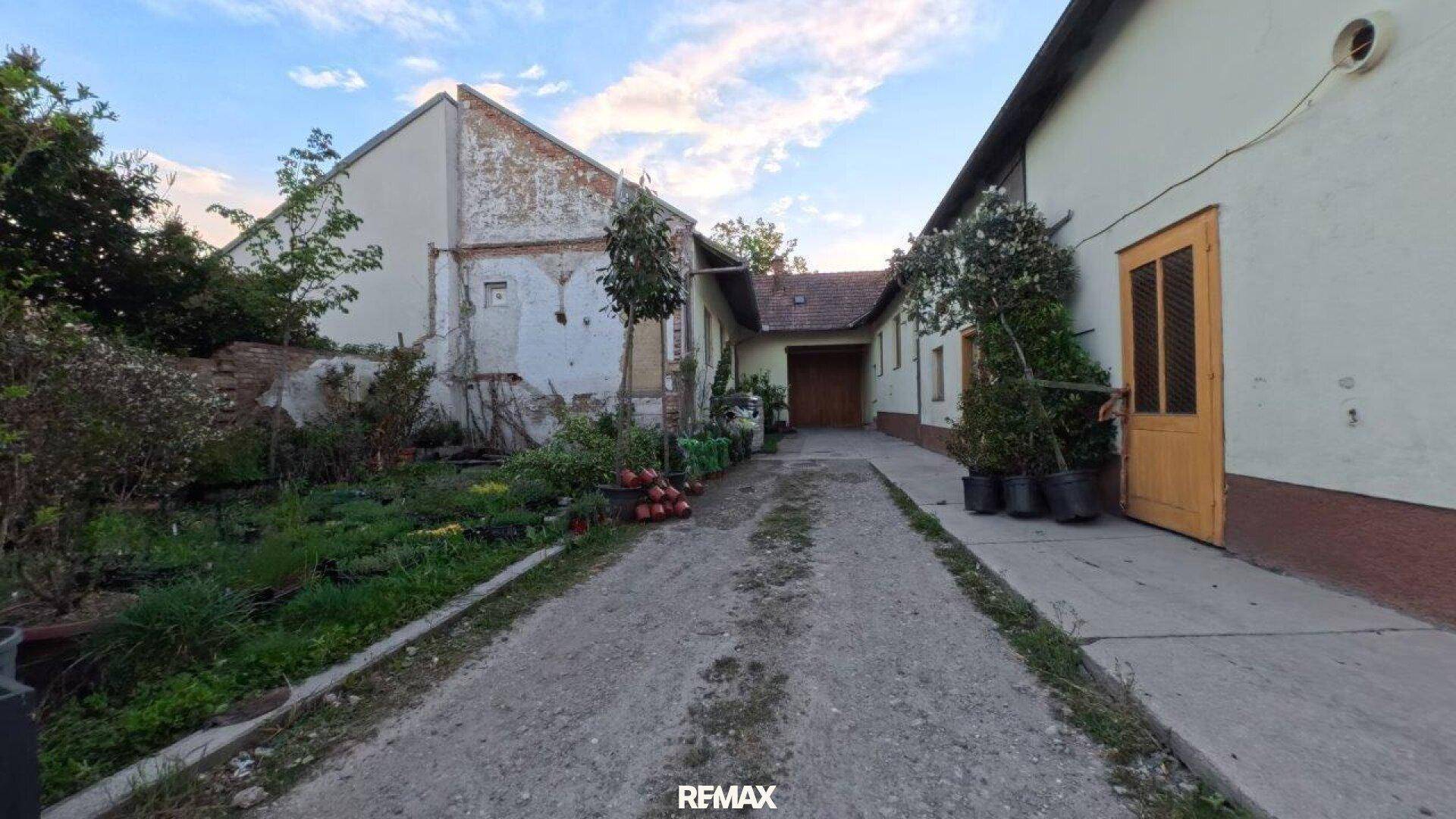 Schotterweg führt zu einem Gebäude, umgeben von einem Gartenbereich mit Pflanzen.