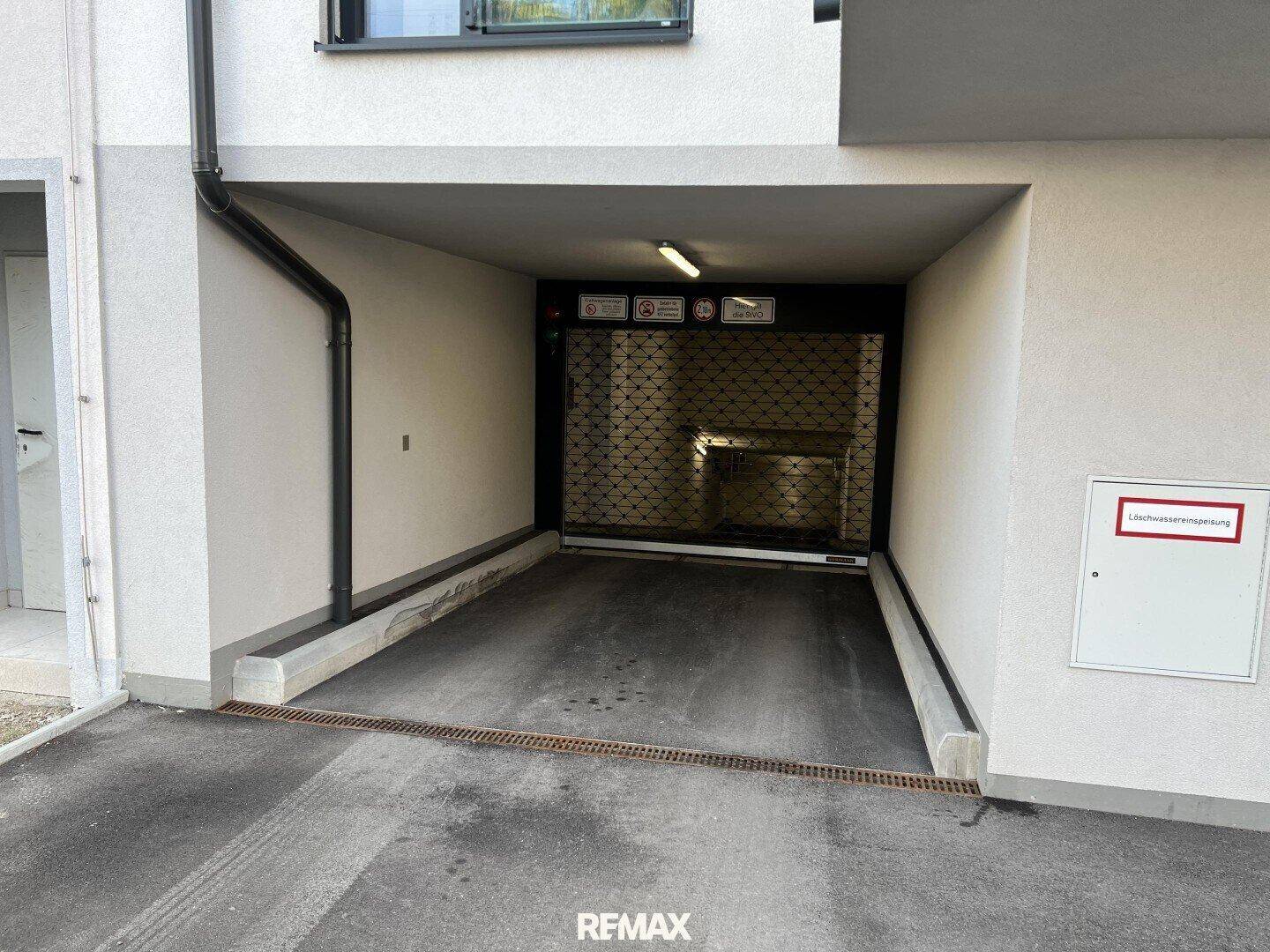 Einfahrt zur Tiefgarage mit geschlossenem Rolltor und moderner Fassadengestaltung.