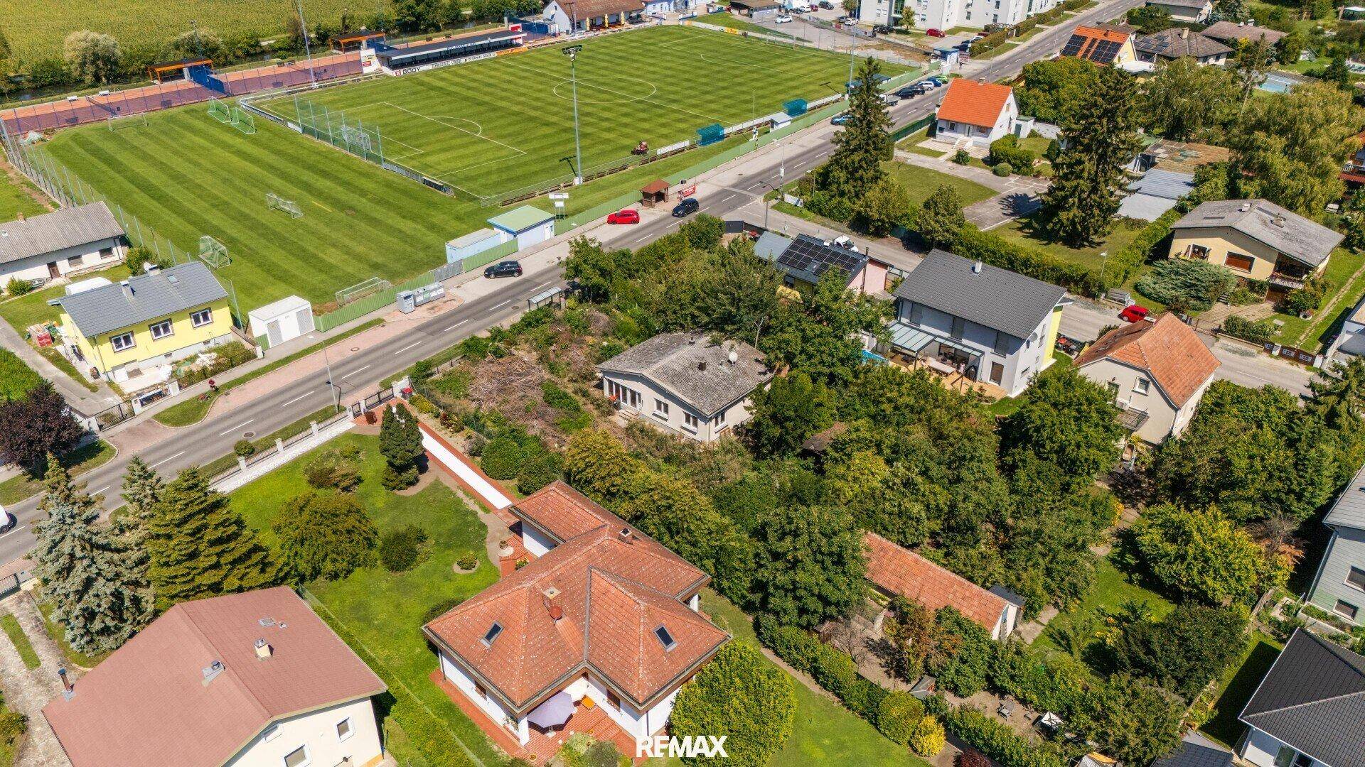 Weitwinkel-Luftaufnahme des Grundstücks mit dem Bestandsgebäude und angrenzendem Sportplatz.