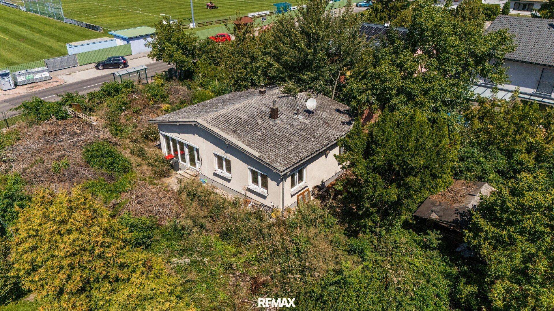 Das Einfamilienhaus aus der Vogelperspektive, umgeben von üppiger Vegetation und mit Blick auf einen Sportplatz.