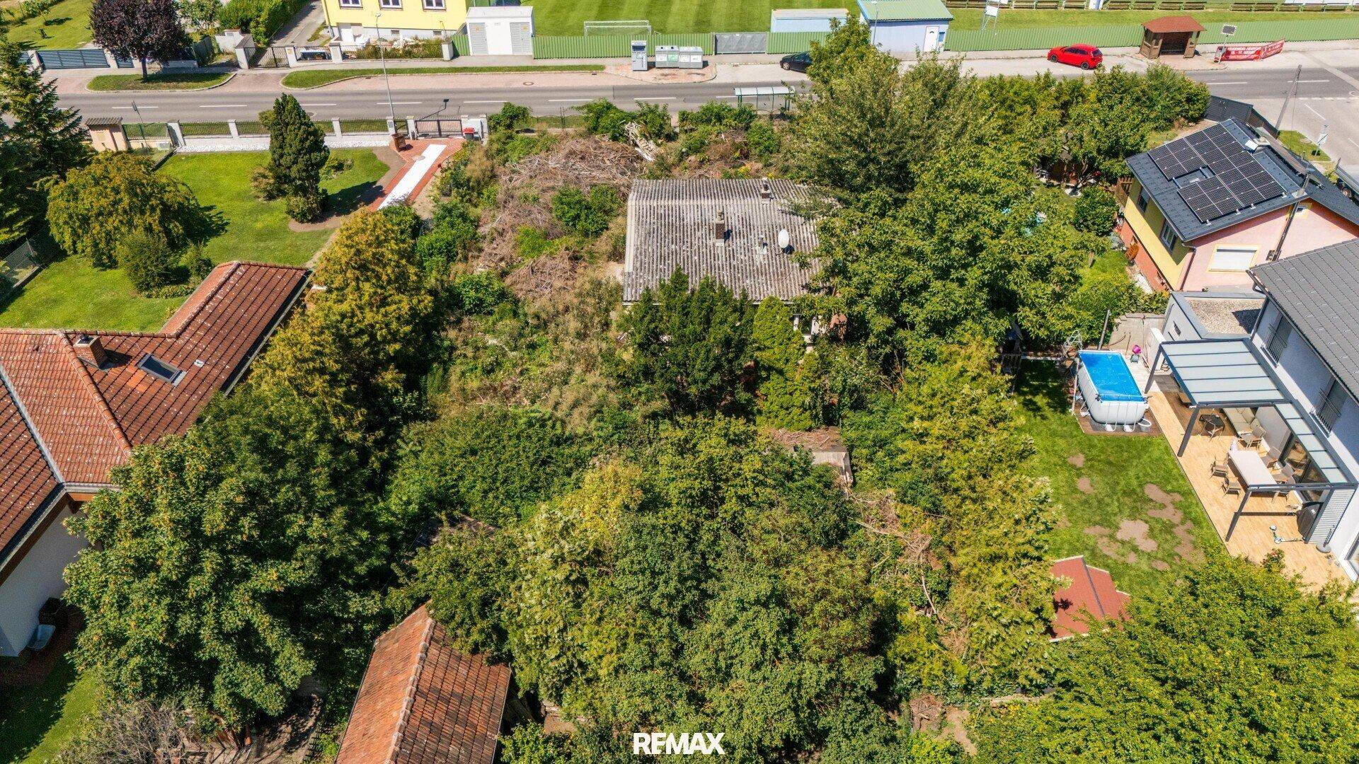 Luftaufnahme des Grundstücks mit einem kleinen Gebäude und viel Bewuchs, angrenzend an einen Sportplatz.
