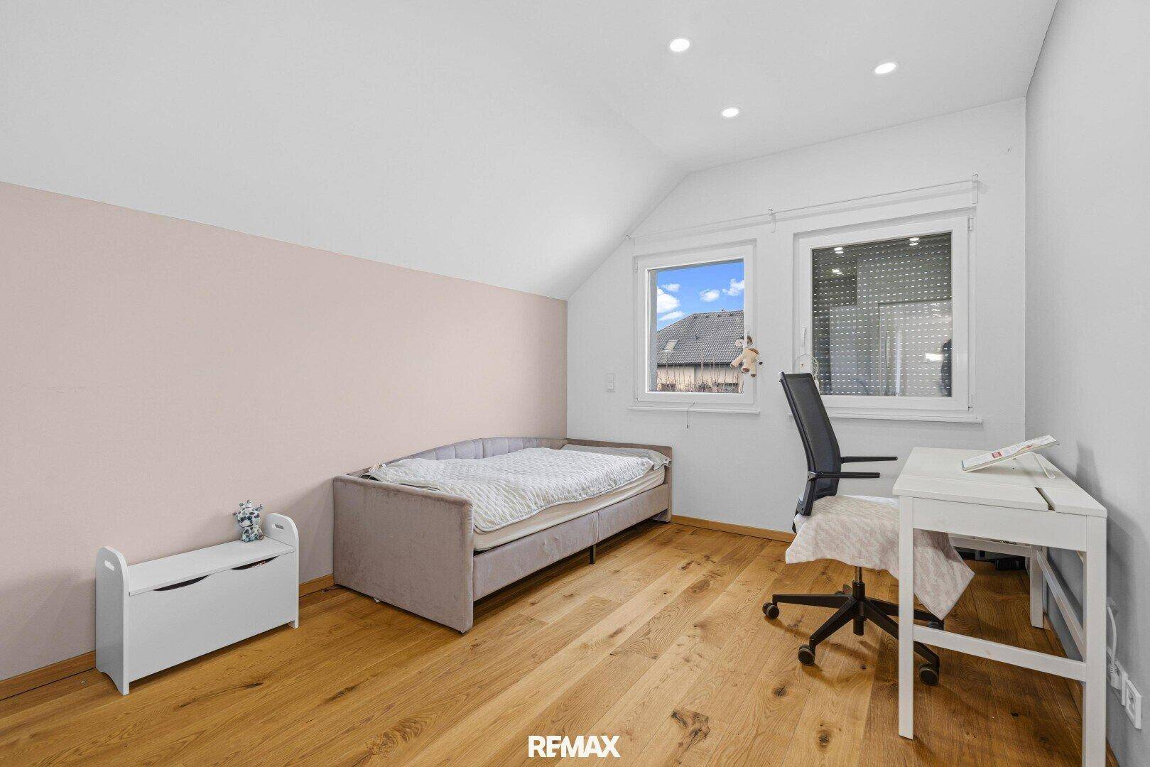 Helles Kinderzimmer mit Einzelbett, Holzboden, rosa Akzentwand und Dachschräge.