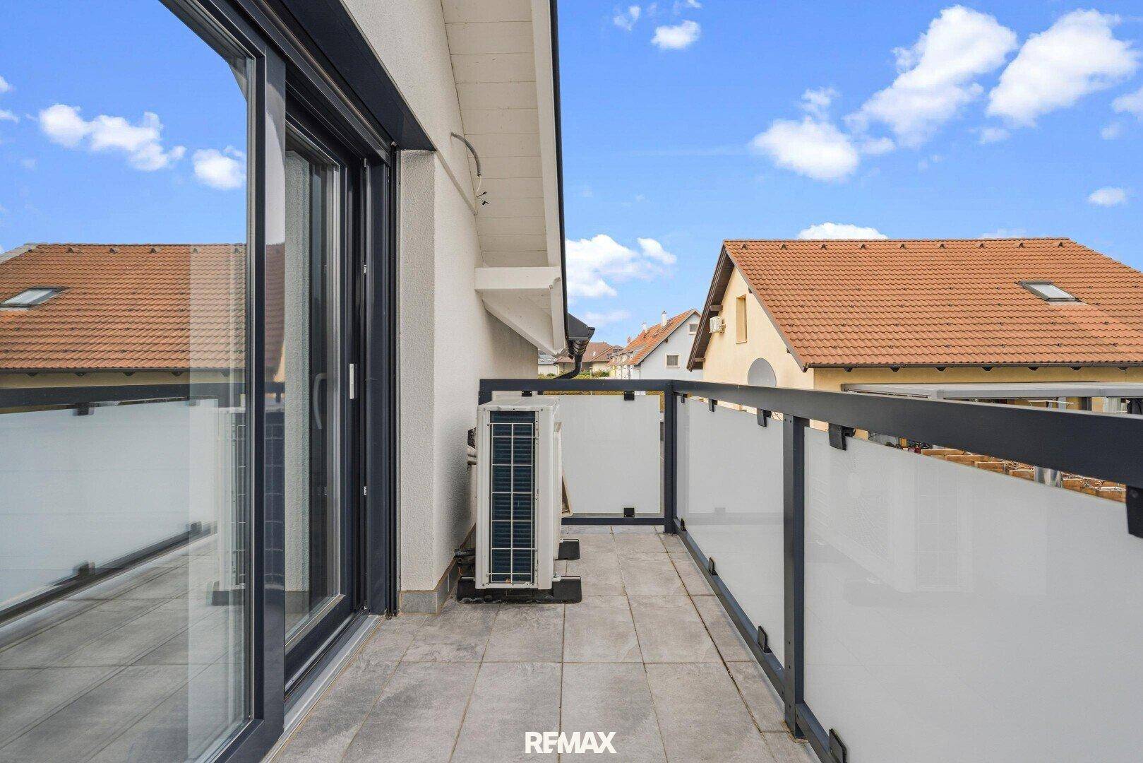 Balkon mit Fliesenboden, Glasgeländer und Blick auf die Umgebung.