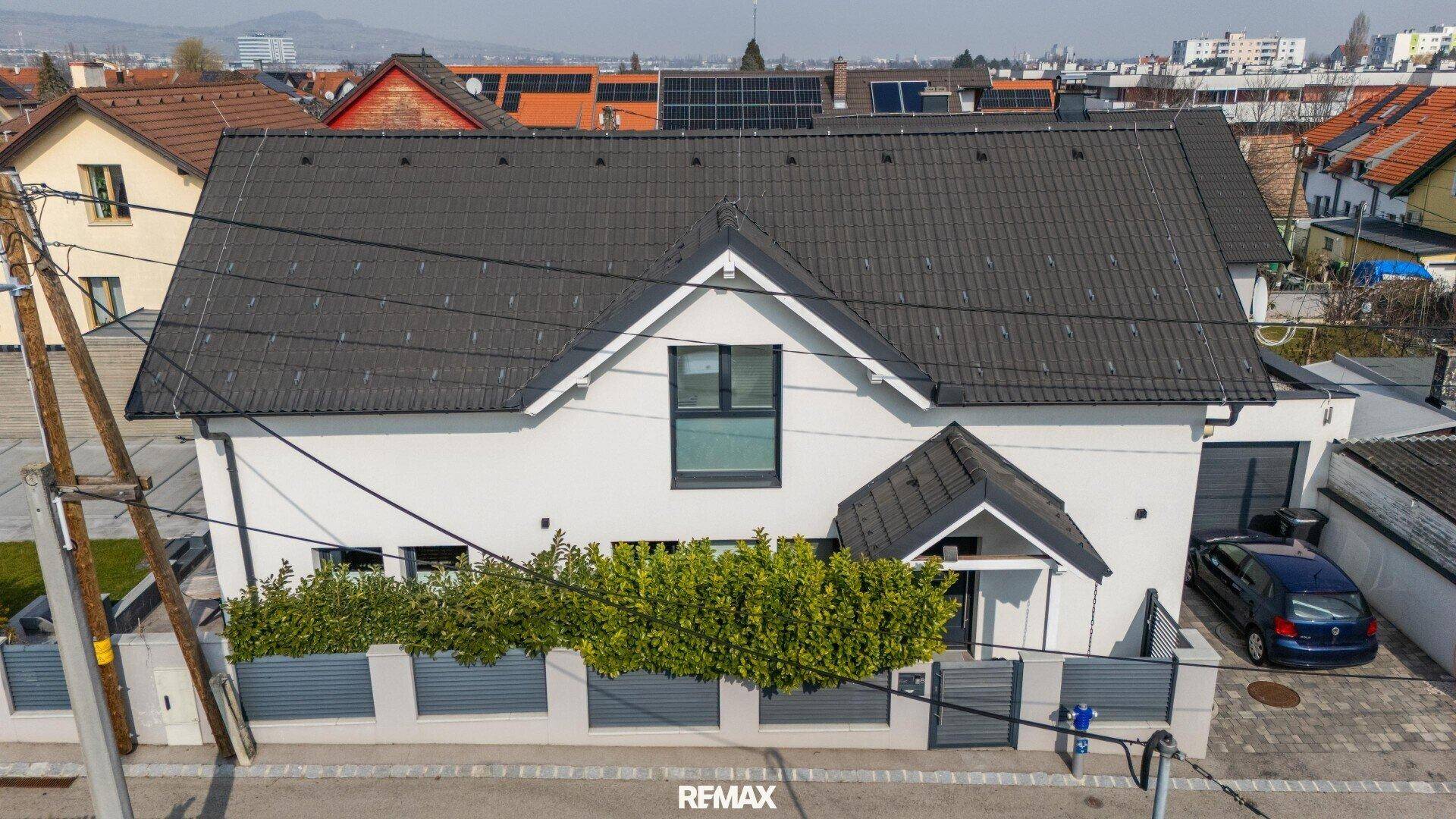 Luftaufnahme der modernen Hausfassade mit Satteldach und umliegender Bebauung.