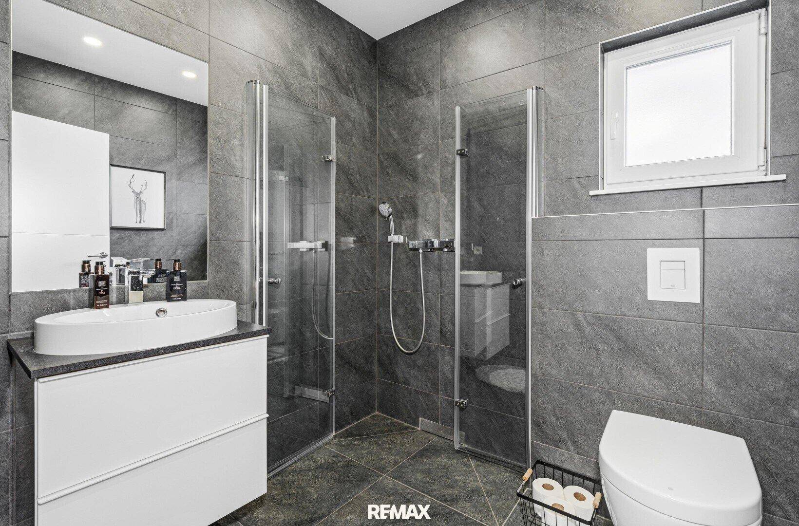Modernes Badezimmer mit dunklen Fliesen, ebenerdiger Dusche und Fenster.