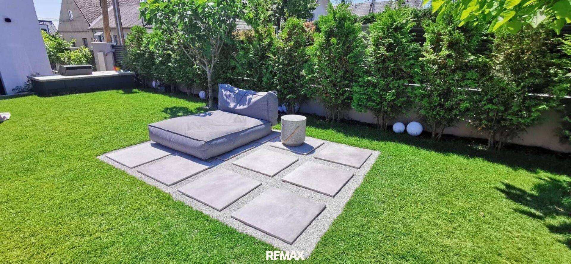 Gepflegter Garten mit Rasenfläche, Trittplatten und gemütlicher Outdoor-Lounge.