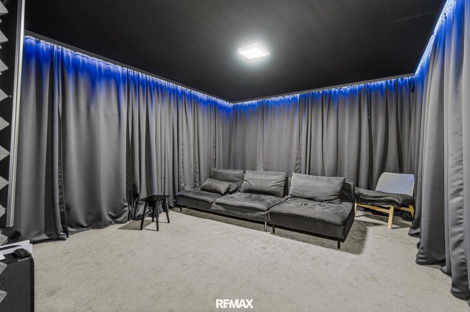 Gemütlicher Medienraum mit dunklen Vorhängen, blauer LED-Beleuchtung und großem Sofa.