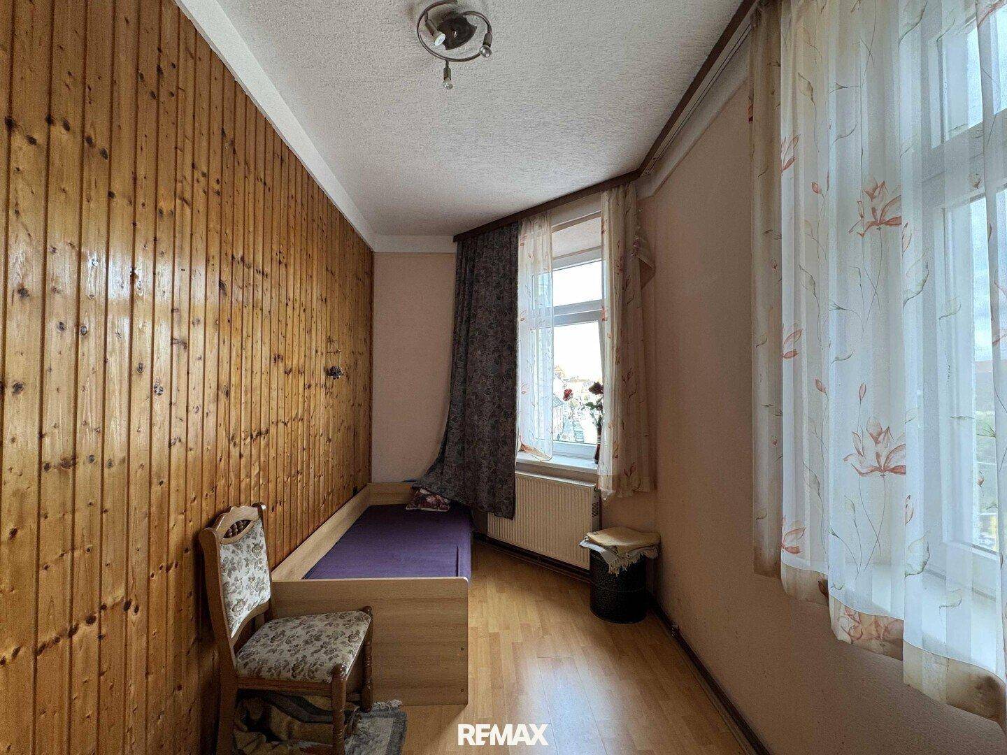Helles Schlafzimmer mit Holzpaneelen, Einzelbett und Fenster mit Vorhängen.