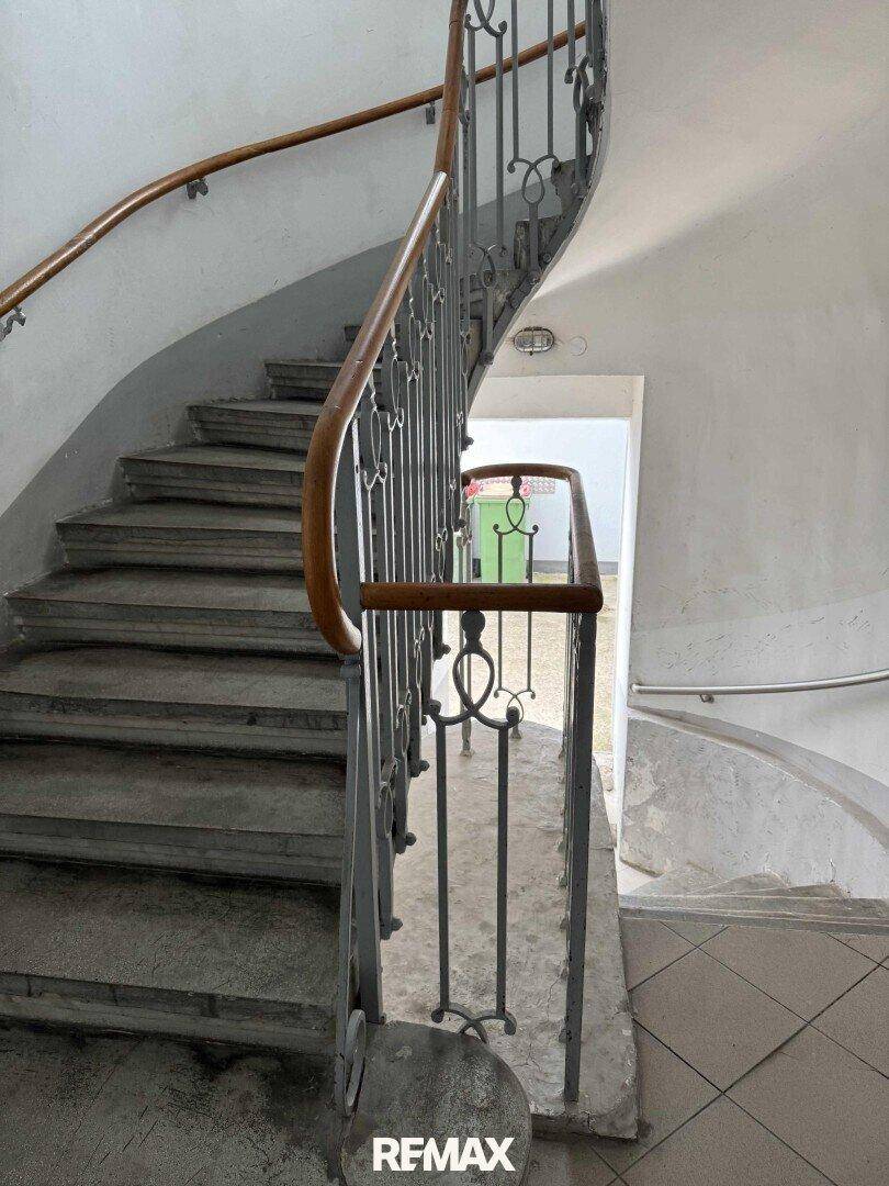Historisches Treppenhaus mit geschwungenem Geländer und Steinstufen.
