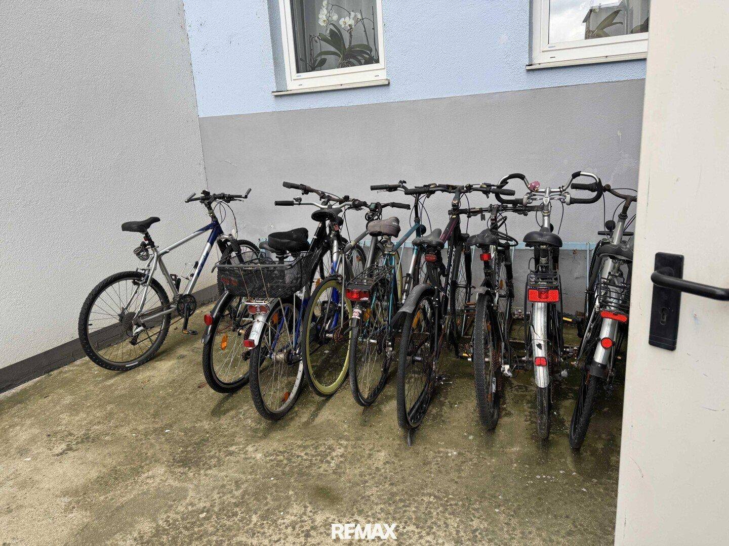 Fahrradabstellplatz im Freien mit mehreren Fahrrädern vor einer Gebäudewand.