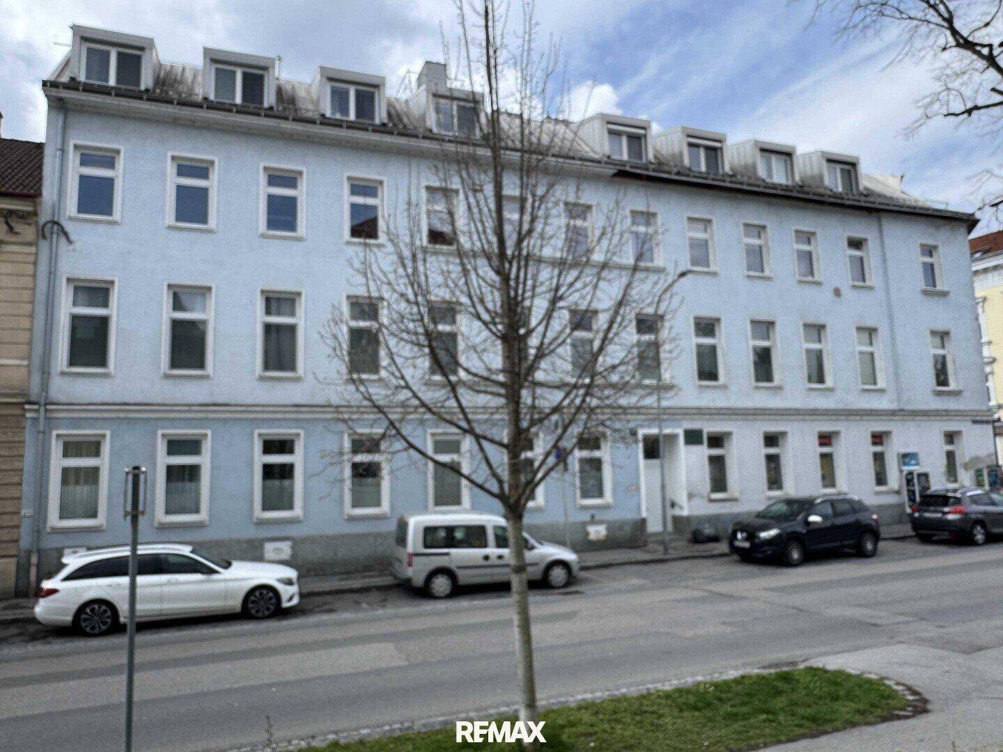 Mehrfamilienhaus mit blauer Fassade und vielen Fenstern an einer städtischen Straße.
