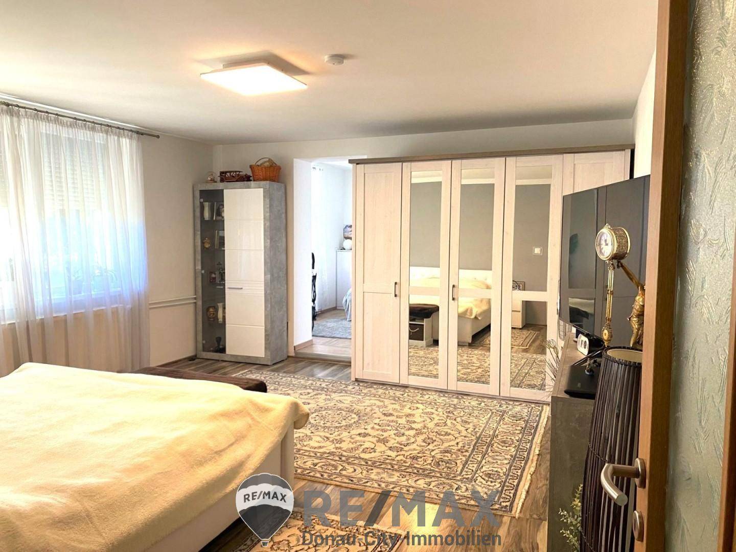 Geräumiges Schlafzimmer mit großem Spiegelschrank, Teppich und hellem Laminatboden.