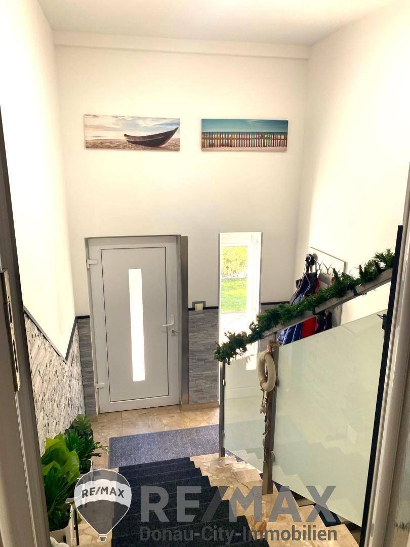 Heller Eingangsbereich mit Treppe, Glasgeländer und moderner Haustür.