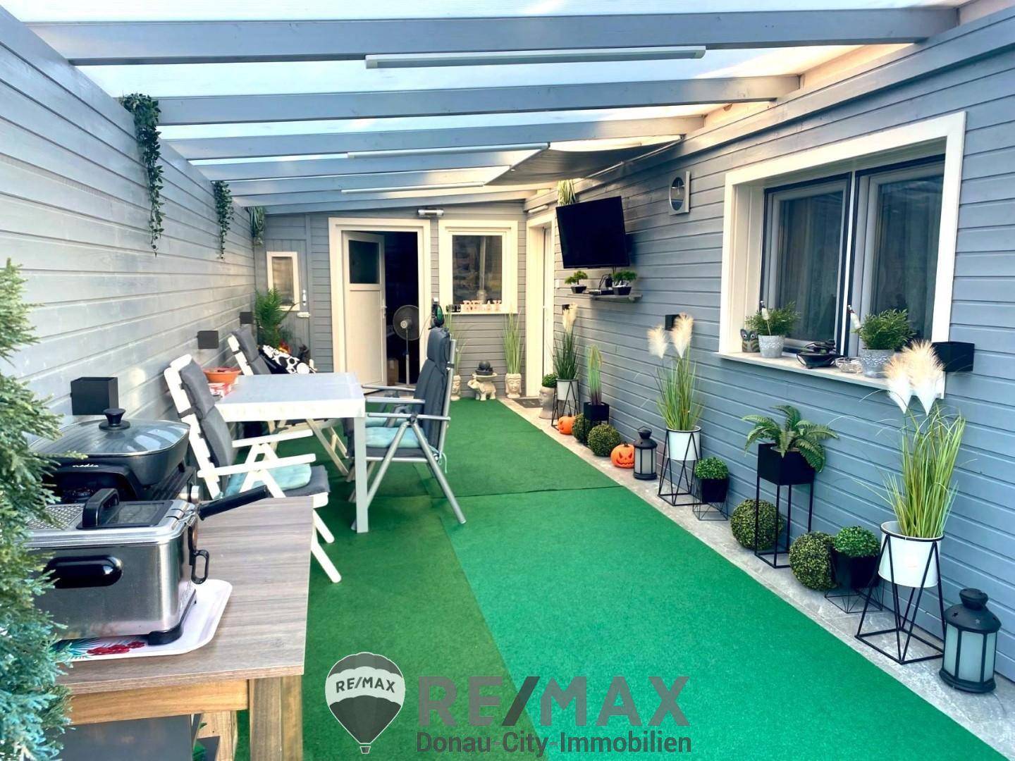 Überdachte Terrasse mit Kunstrasen, Esstisch und Dekoration, ideal für entspannte Stunden im Freien.