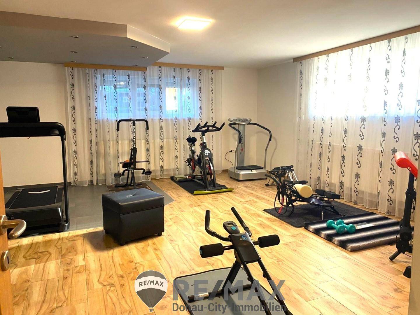 Geräumiger Fitnessraum mit verschiedenen Trainingsgeräten und hellem Holzboden.