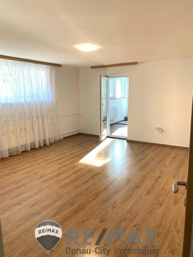 Helles Zimmer mit Laminatboden, Fenster und Zugang zu einem weiteren Raum.